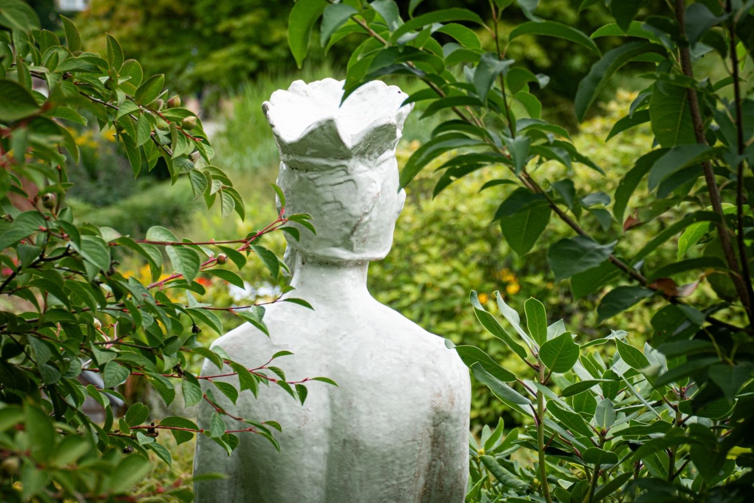 Weiße Figur mit Krone zwischen Sträuchern – Stimmungsbild innerer Garten