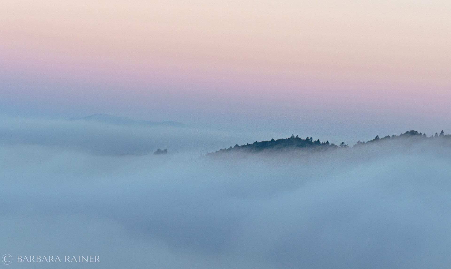 Nebel über einer Hügellandschaft unter einem zartrosa Morgenhimmel