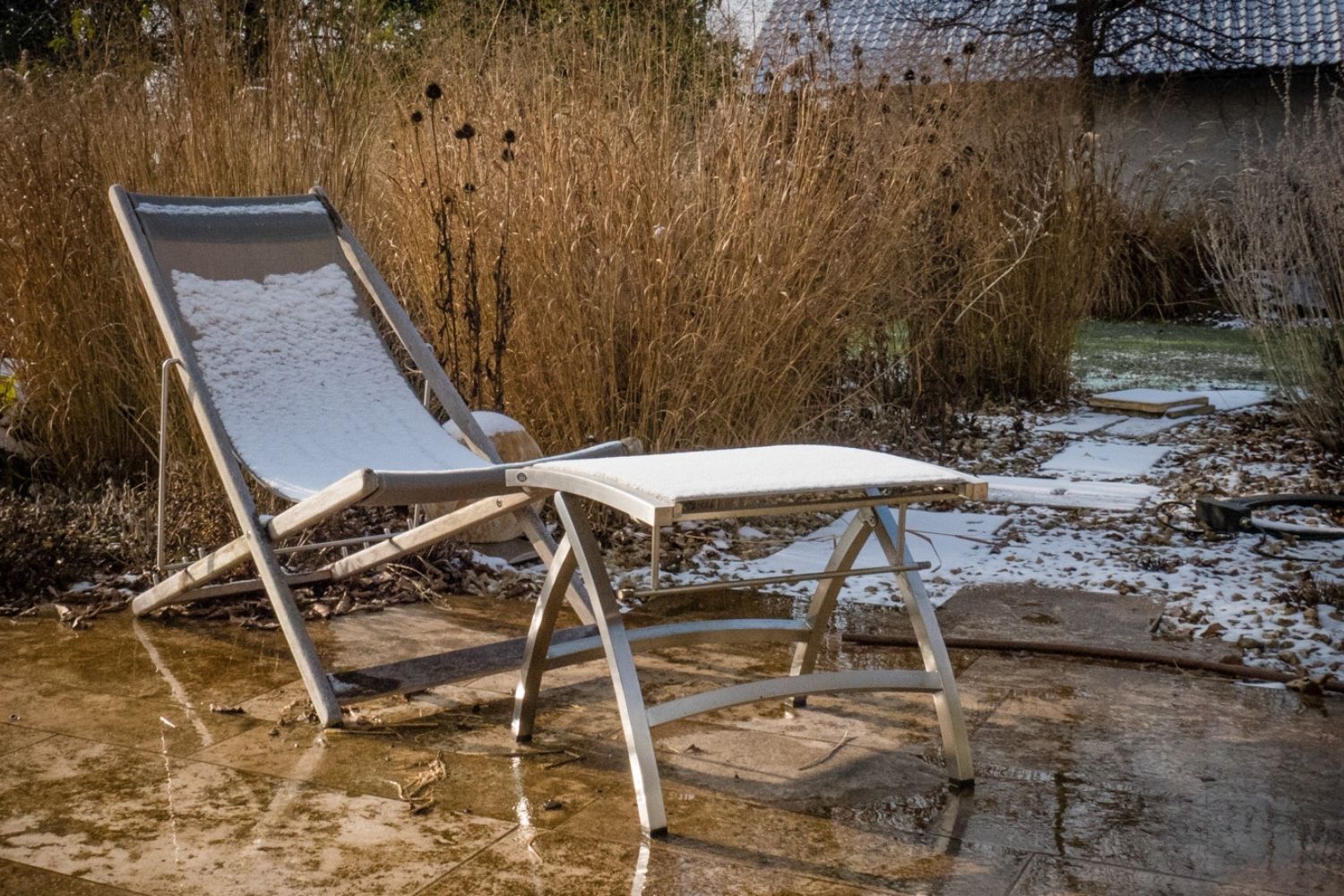 Liegestuhl im Schnee vor goldenen Rutenhirse-Halmen im Winter