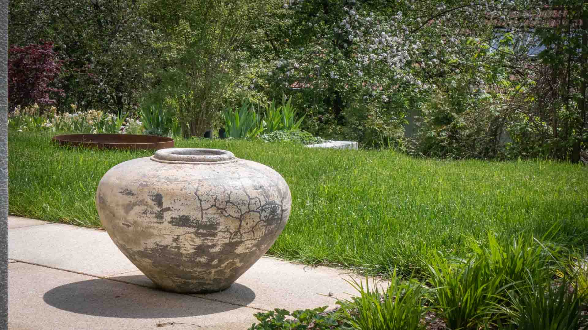 Großes Gefäß in einem üppig bepflanzten Garten mit klarer räumlicher Ordnung