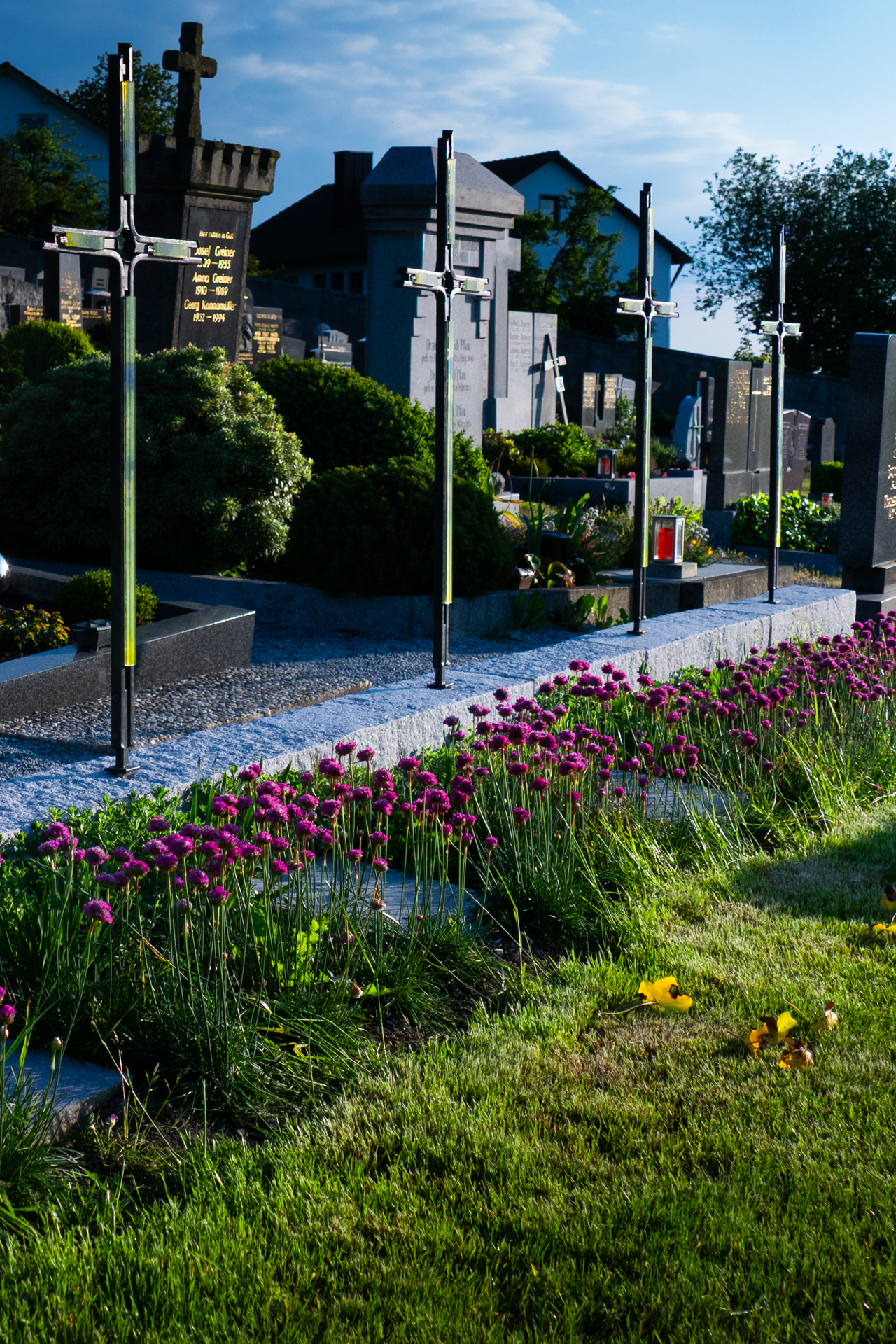 Friedhofsraum mit Gräbern, Kreuzstelen und blühender Bepflanzung als gelebter Ort.