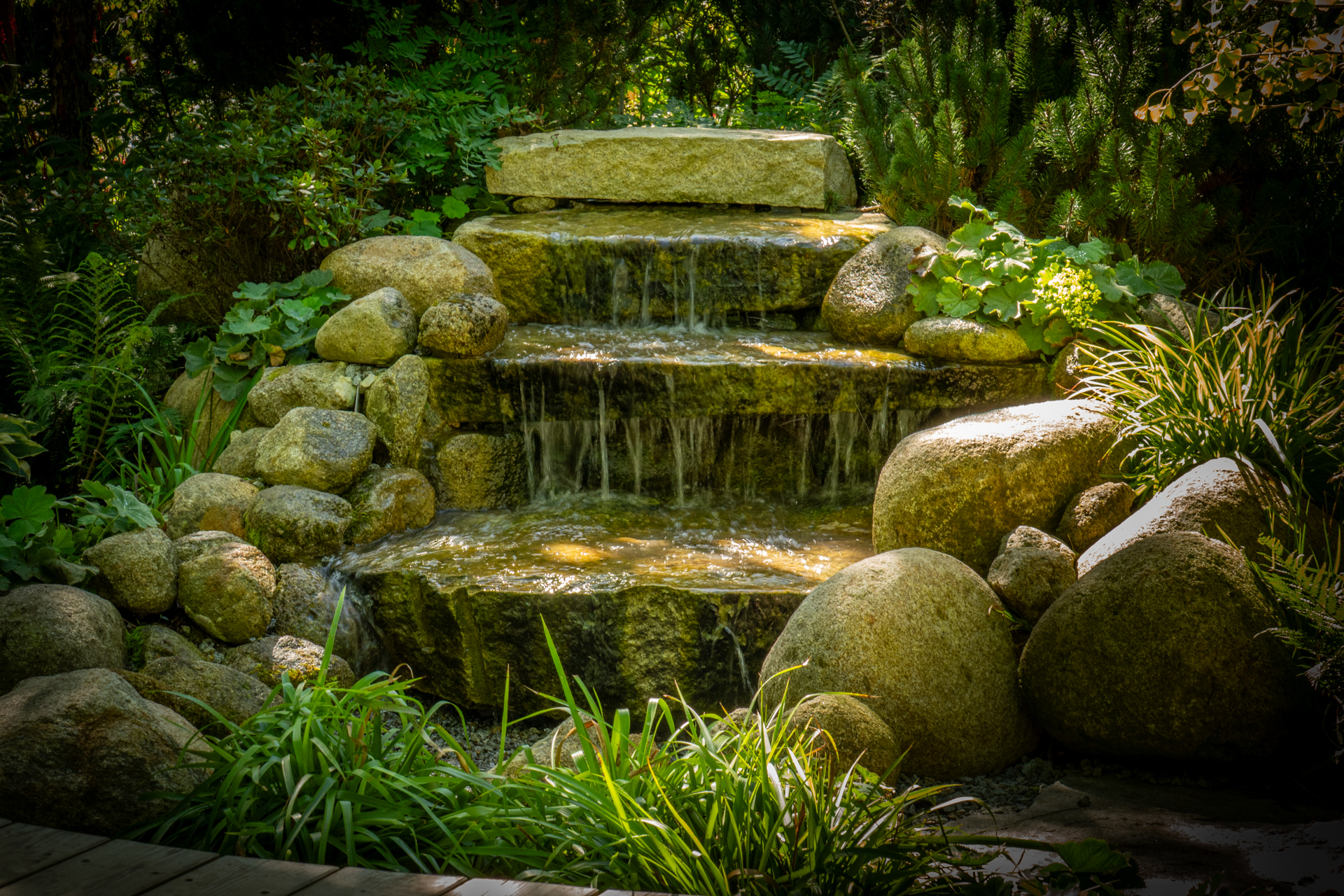 Naturnahes Wasserelement im Garten – ein moosbewachsener Quellstein mit klarem Wasser, umgeben von Stauden